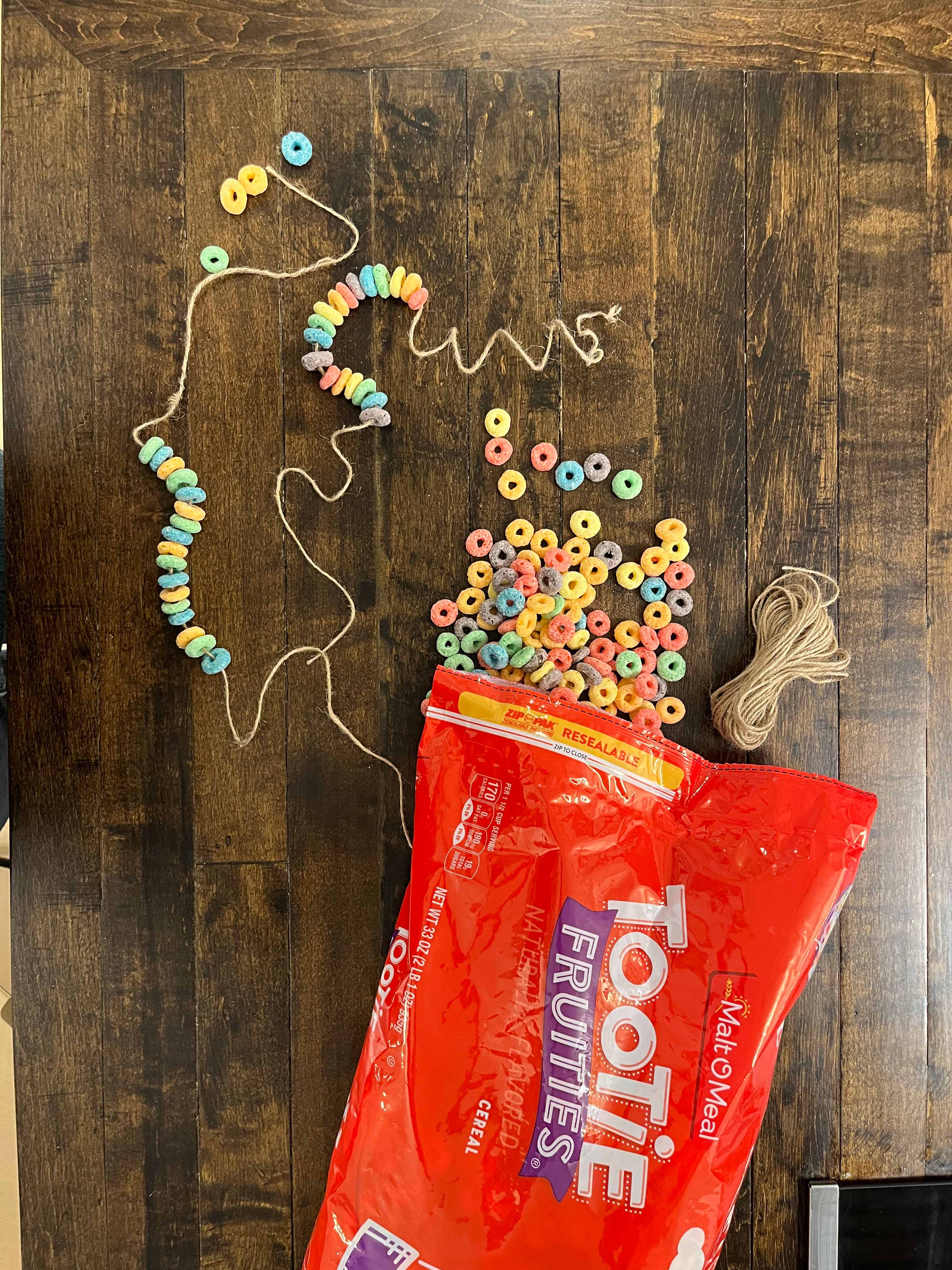 A necklace strung with Tootie Fruities cereal. An open bag of Tootie Fruities is nearby.