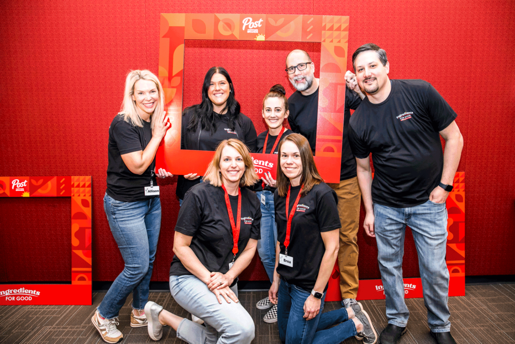 Post employees in black shirts pose for a photo against a red wall