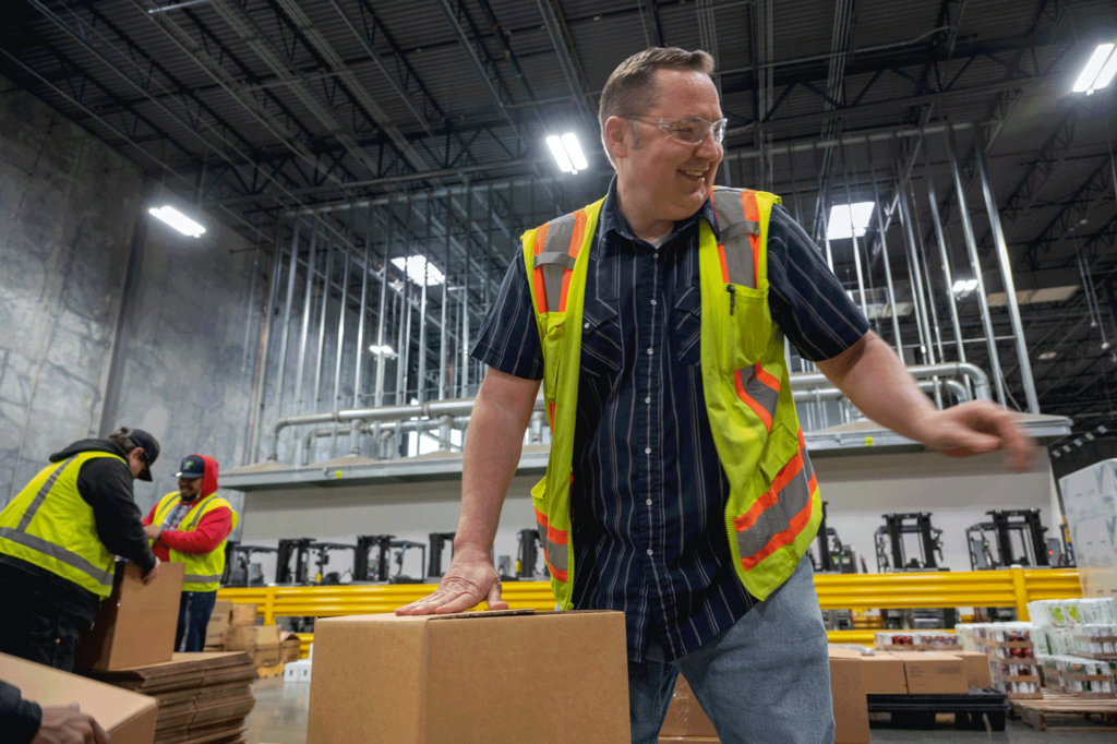A man in a safety jacket and glasses moves boxes